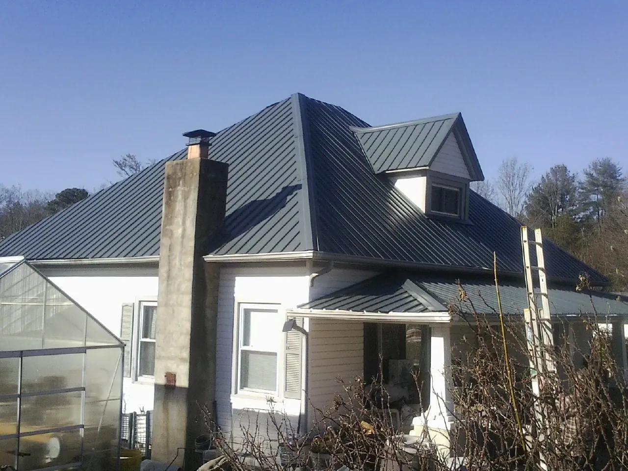 Dark blue standing seam metal roof on a white farmhouse with dormer — Slate & Tile Roof Repair by Roofing Brothers in Polaris