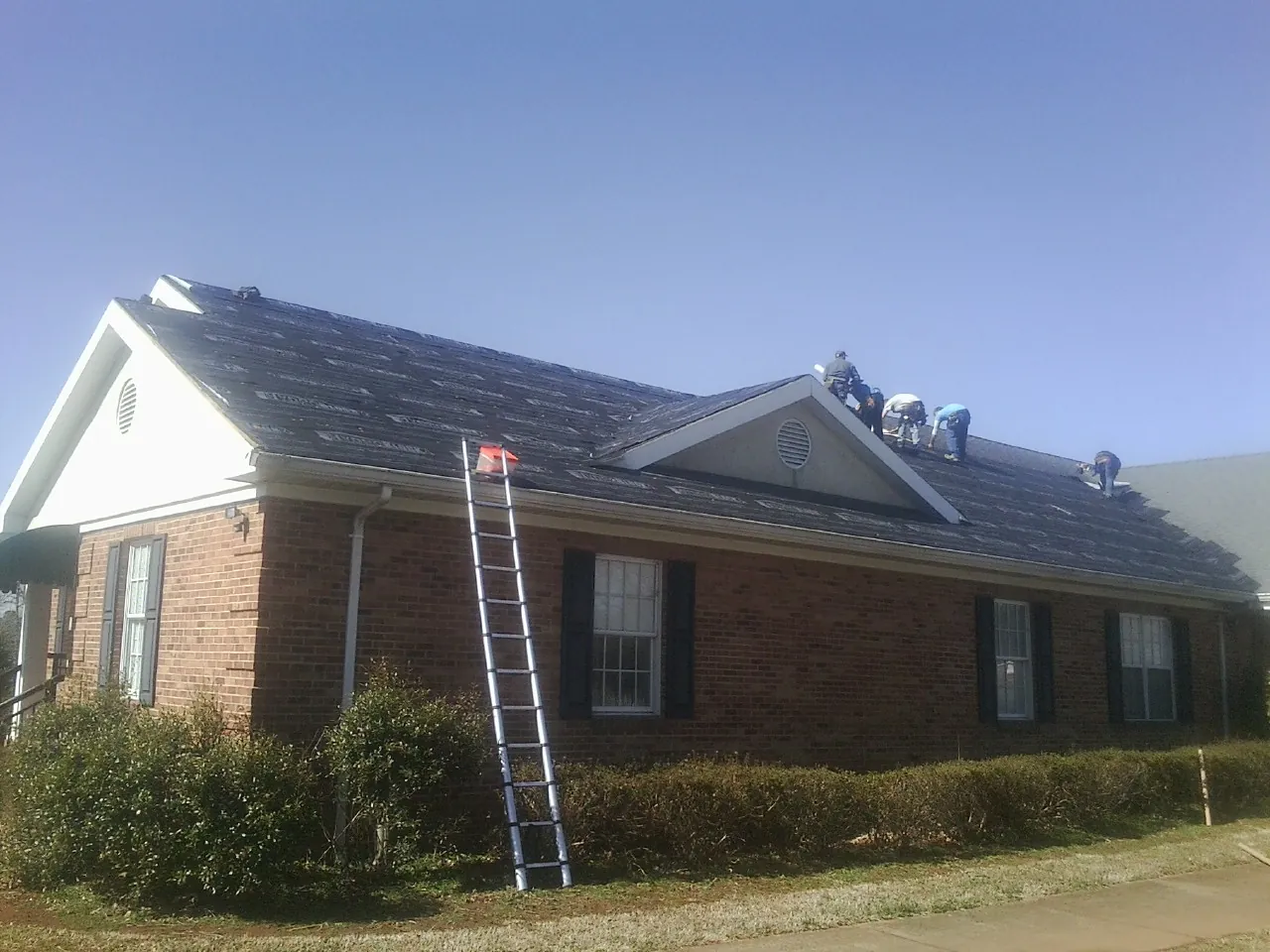 Crew tearing shingles off a brick ranch roof with a ladder set — Emergency Roof Repair work by our crew in Polaris