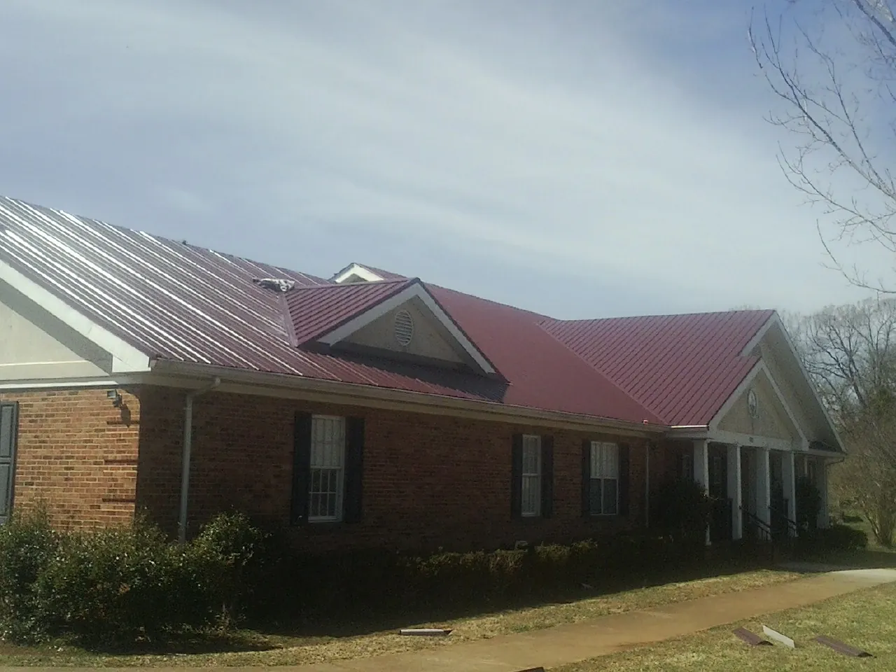 Red metal roof with gabled entries on a long brick building, from a Hail Damage Roof Repair job in Polaris