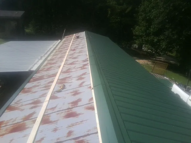 Old rusted panels beside newly installed green metal roofing — Wind Damage Roof Repair by Roofing Brothers in Polaris