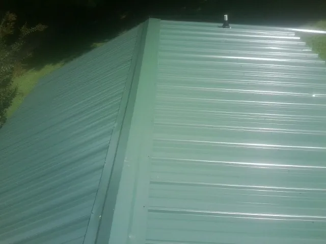 New green metal panels meeting at the ridge of a roof — Flat Roof Repair work by our crew in Polaris