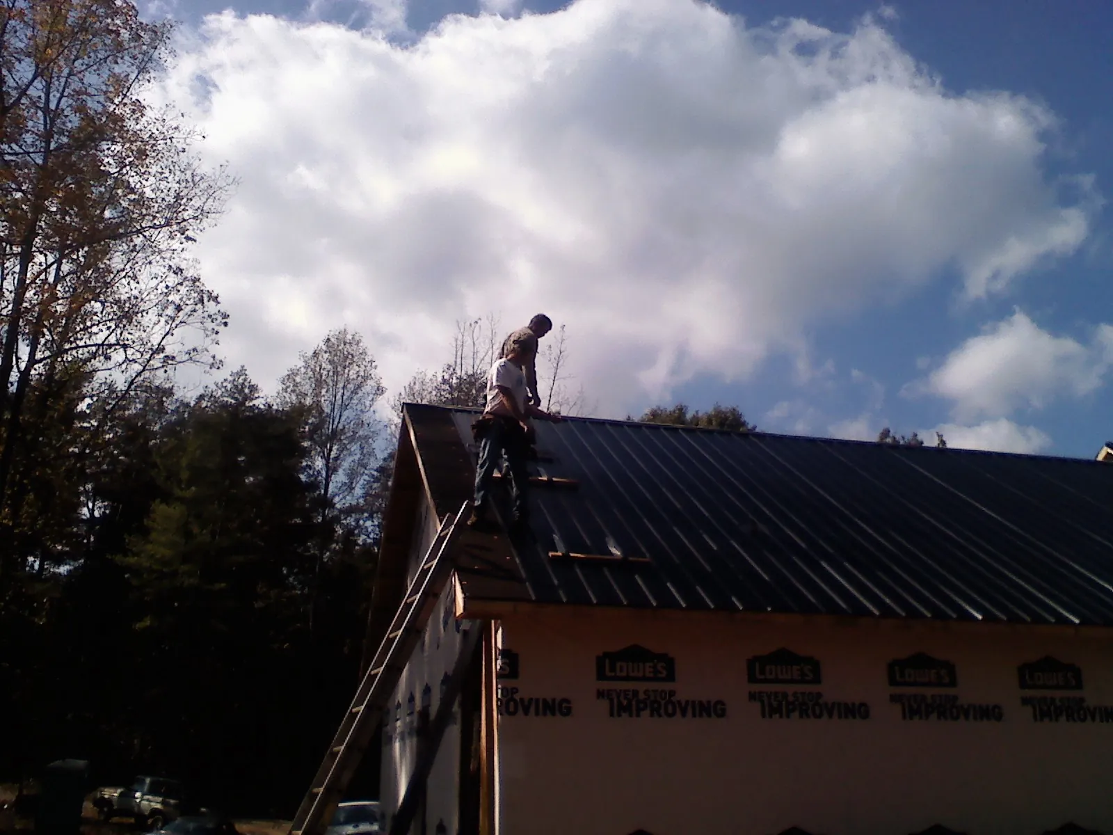 Roofer fastening dark metal panels high against a cloudy sky, from a Roof Inspection job in Polaris