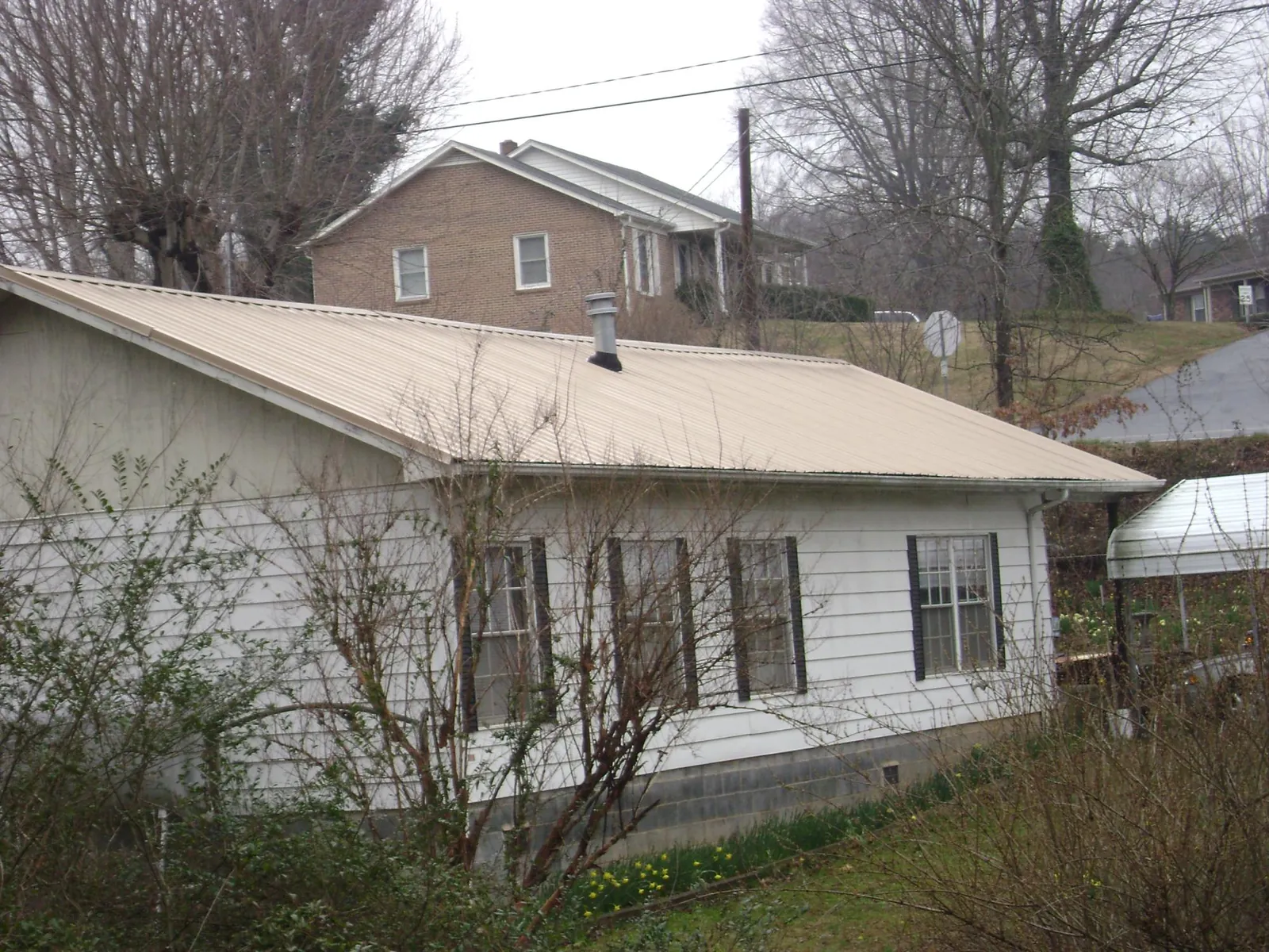 Tan metal roof on a white sided house set into a hillside — Commercial Roofing by Roofing Brothers in Polaris